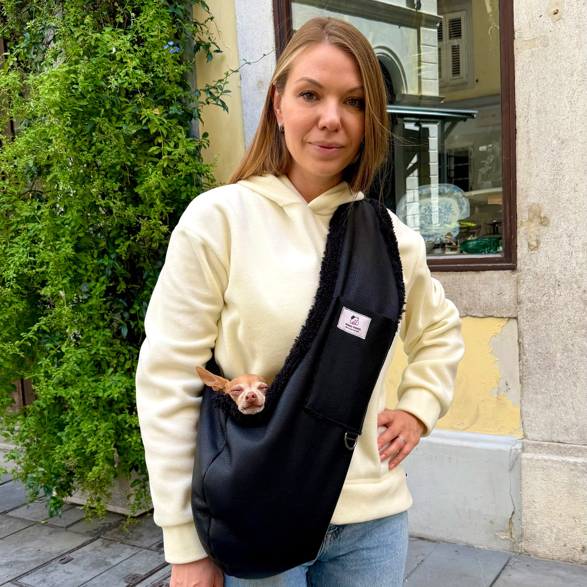 Woman wearing the Aspen black dog sling carrier with a small dog inside