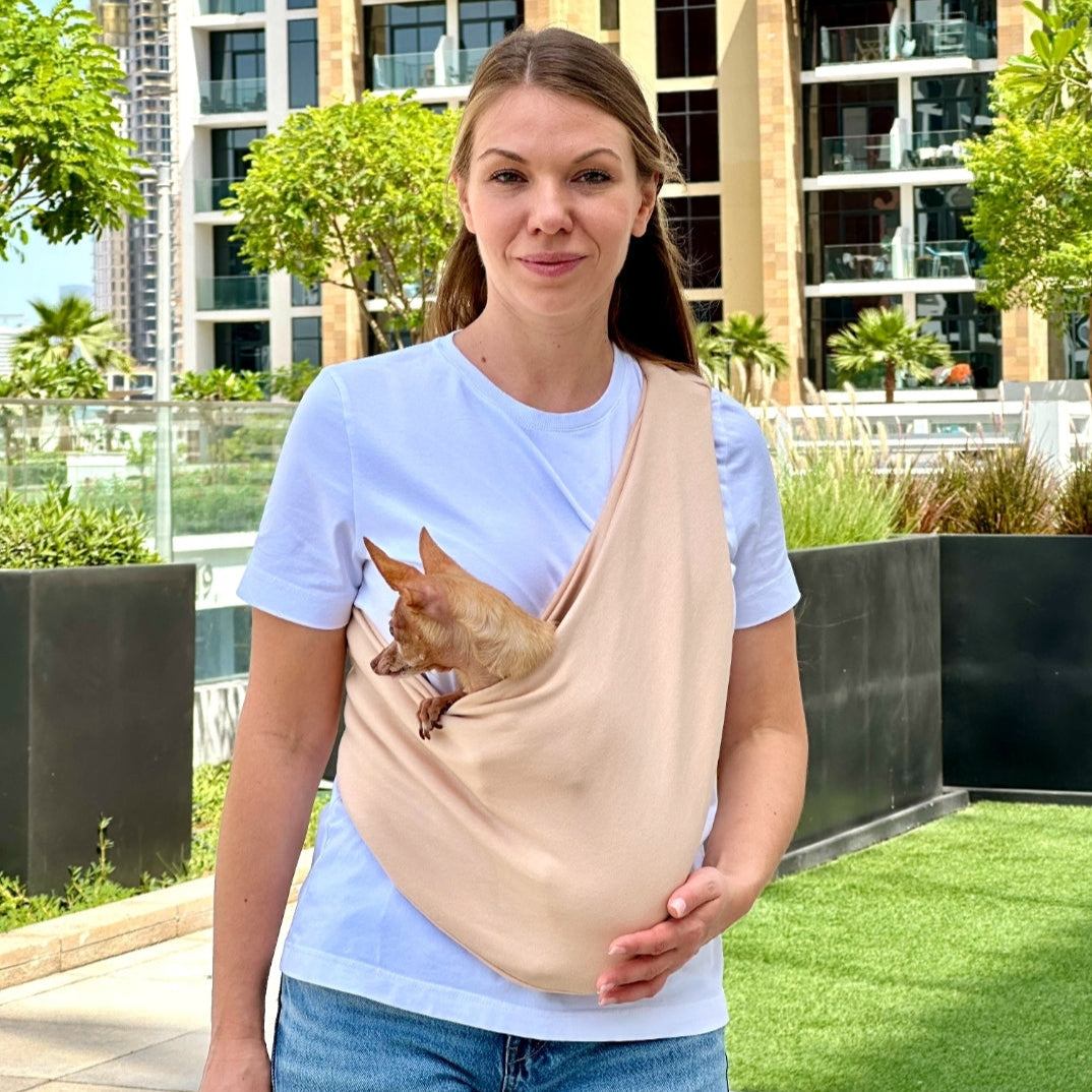 Woman carrying small dog in beige cotton sling carrier