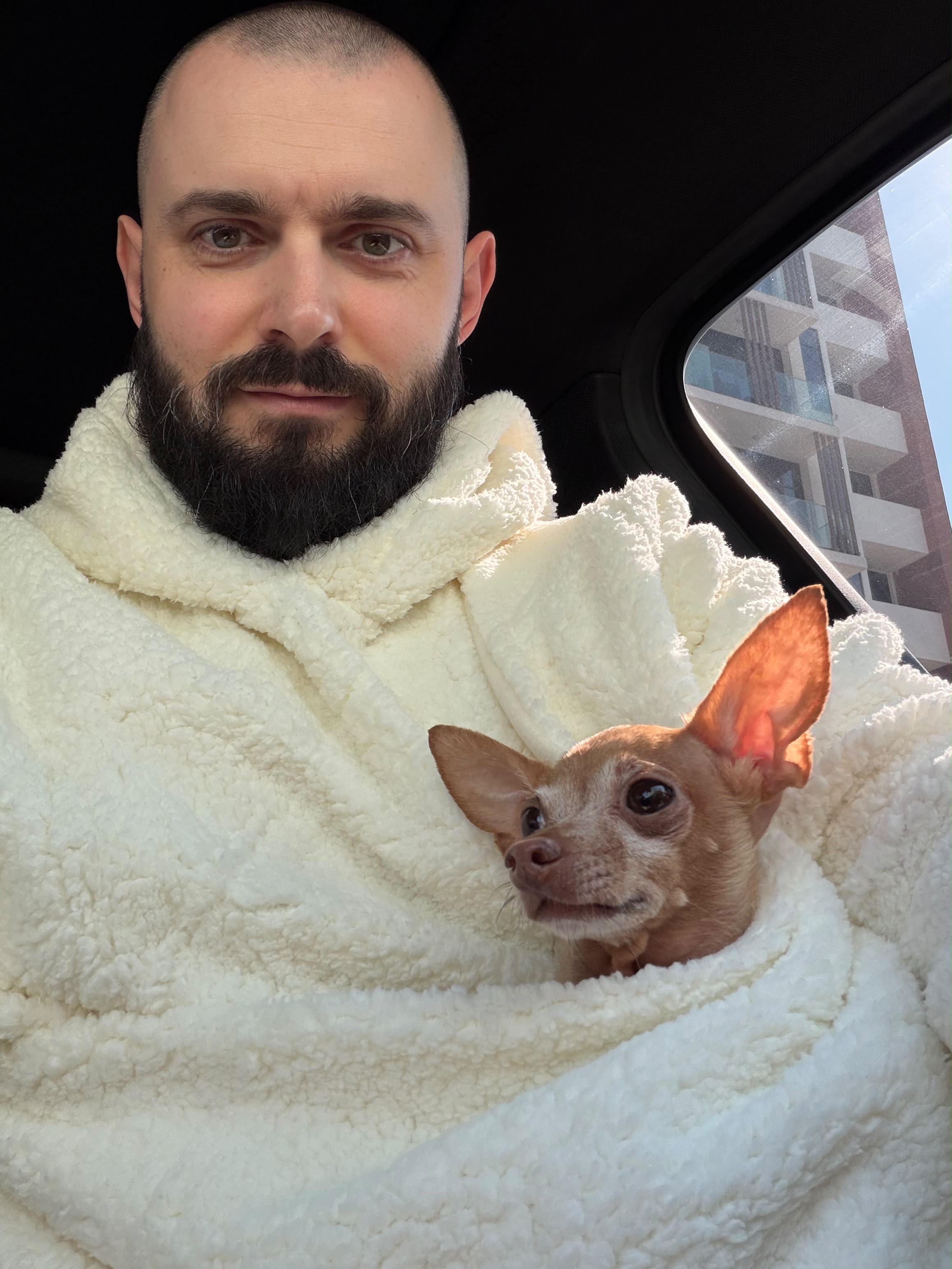 Cristian relaxing in a white Kokopaws Teddy carrier hoodie during a road trip. Cozy hands-free pet carrier for small dogs.